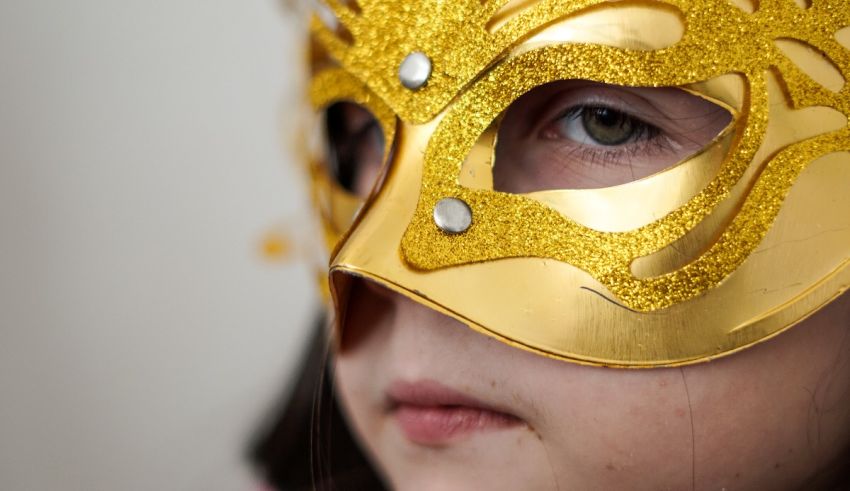 A young girl wearing a gold masquerade mask.