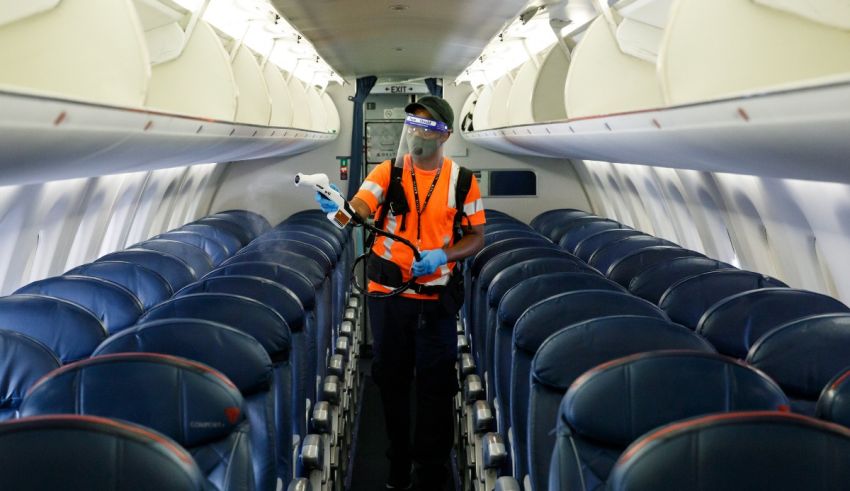 A man in an orange vest is standing in the aisle of an airplane.