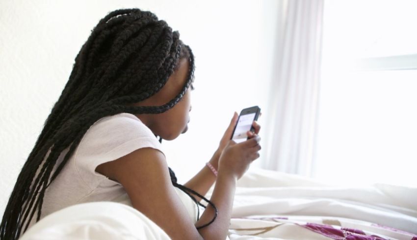 A young woman using a cell phone in bed.