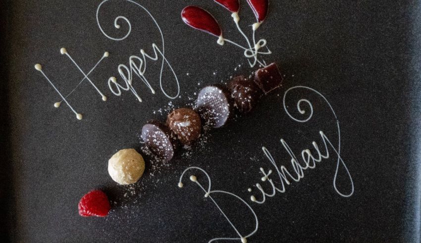 A birthday cake with chocolates and raspberries on a black plate.