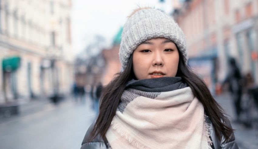 A young asian woman wearing a scarf and hat on the street.