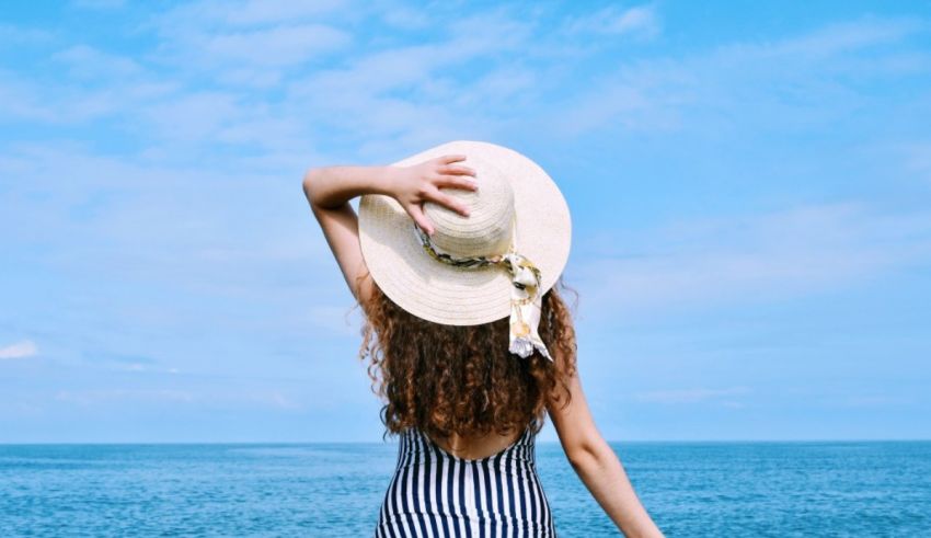 A woman in a striped swimsuit with a hat standing on the beach.