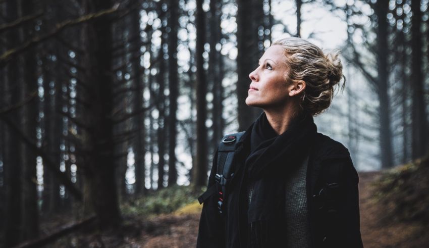 A woman standing in a forest looking up.