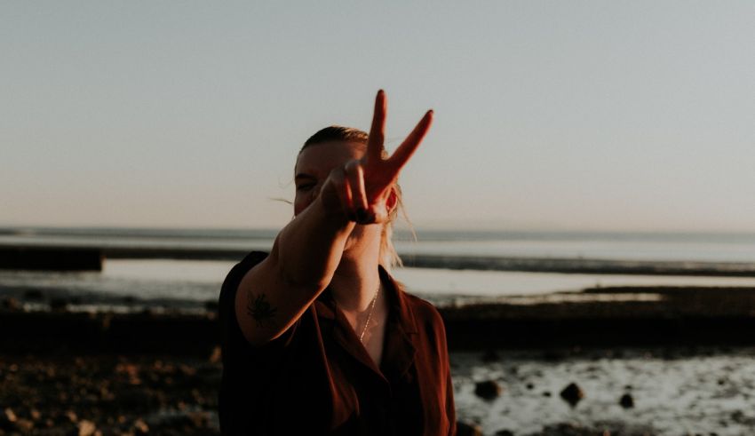 A woman making a peace sign in front of a body of water.