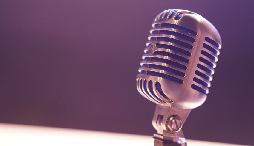 A microphone sits on a table in front of a purple background.