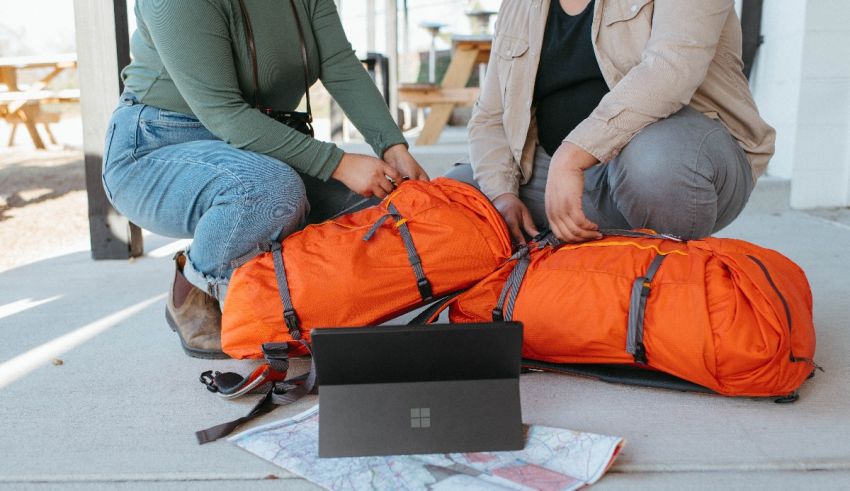 Two people sitting on the ground with luggage and a laptop.