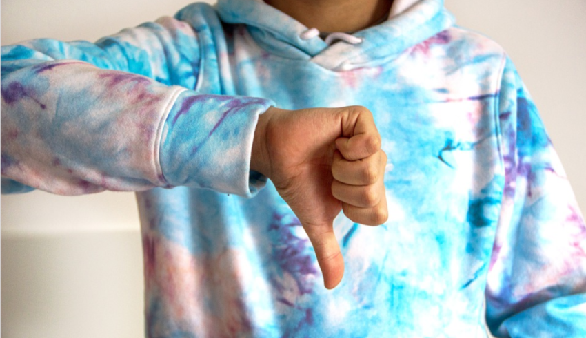 A person wearing a tie dye hoodie showing a thumbs down sign.