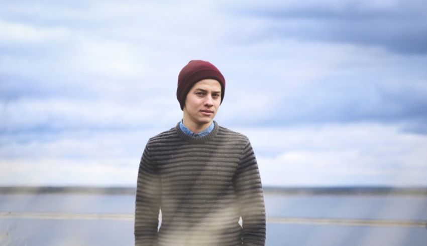 A young man wearing a beanie standing in front of a body of water.