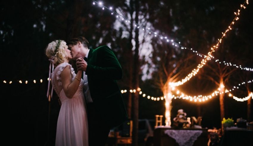 A bride and groom kissing under a string of lights.