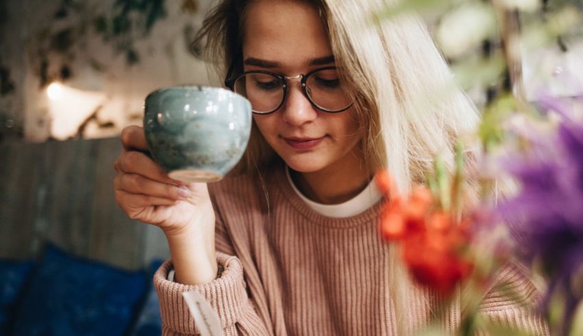 A woman wearing glasses is holding a cup of coffee.