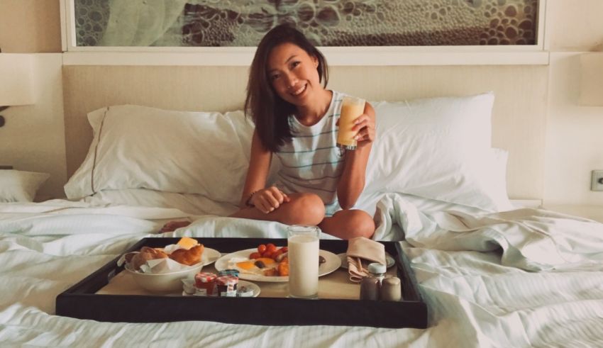 A woman sitting on a bed with a tray of food.