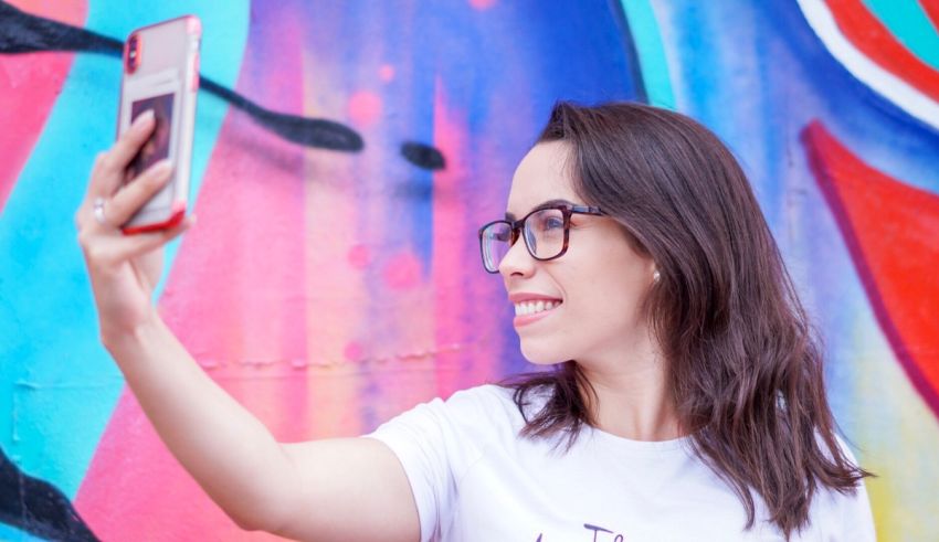 A woman is taking a selfie in front of a colorful wall.