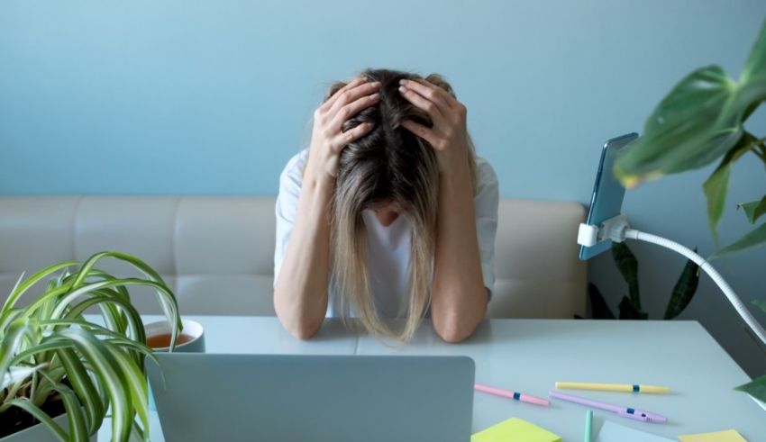 A woman is sitting at a desk with her head in her hands.