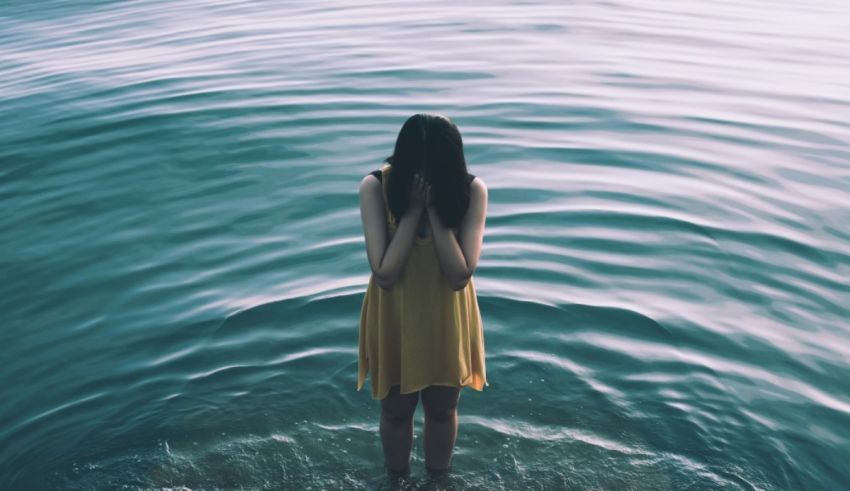 A woman standing in water with her hands over her face.