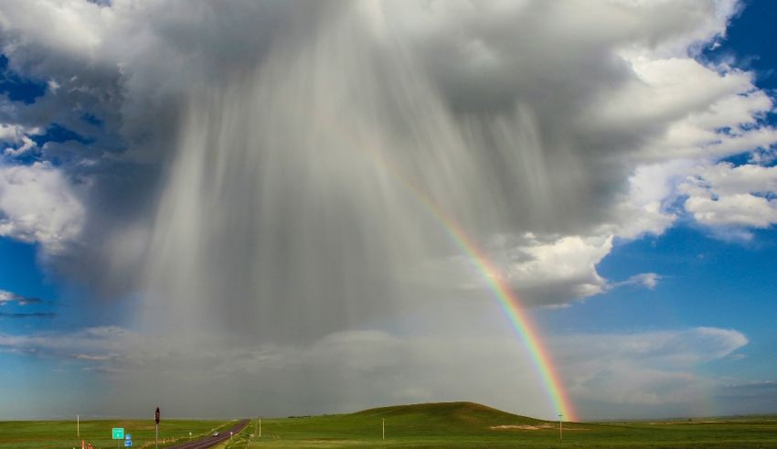 A rainbow falls over a road in the middle of a field.