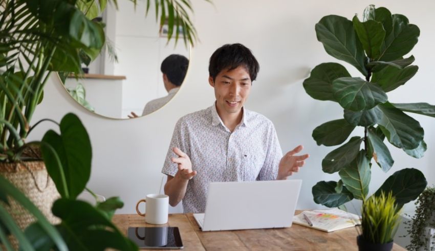 A man sitting at a table with a laptop and plants.