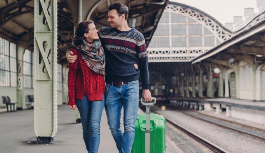 A man and woman holding a green suitcase in a train station.