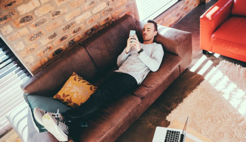 A man is laying on a couch and using a cell phone.