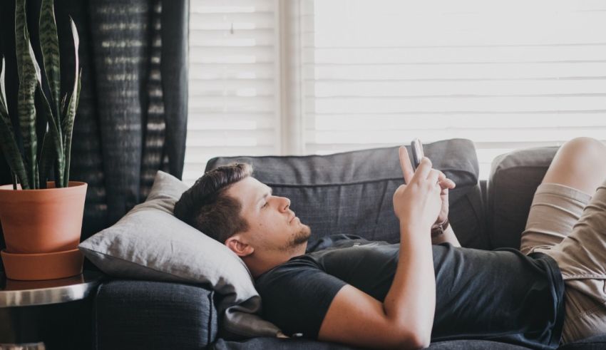 A man laying on a couch and using his cell phone.