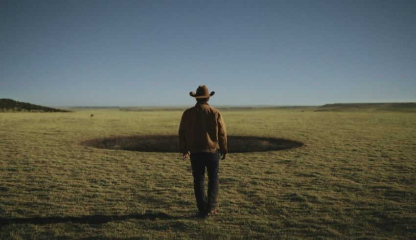 A man in a cowboy hat standing in a field with a hole in it.