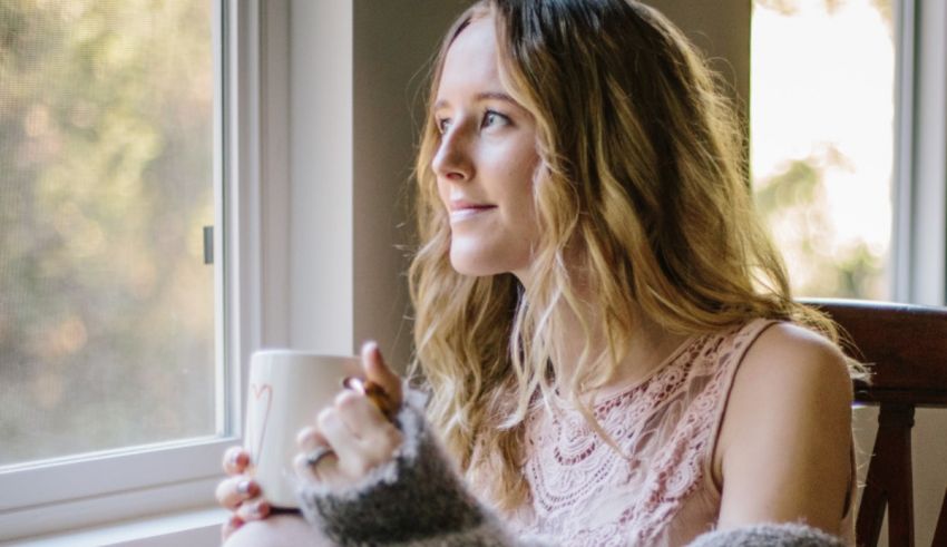 A woman looking out a window while holding a coffee mug.