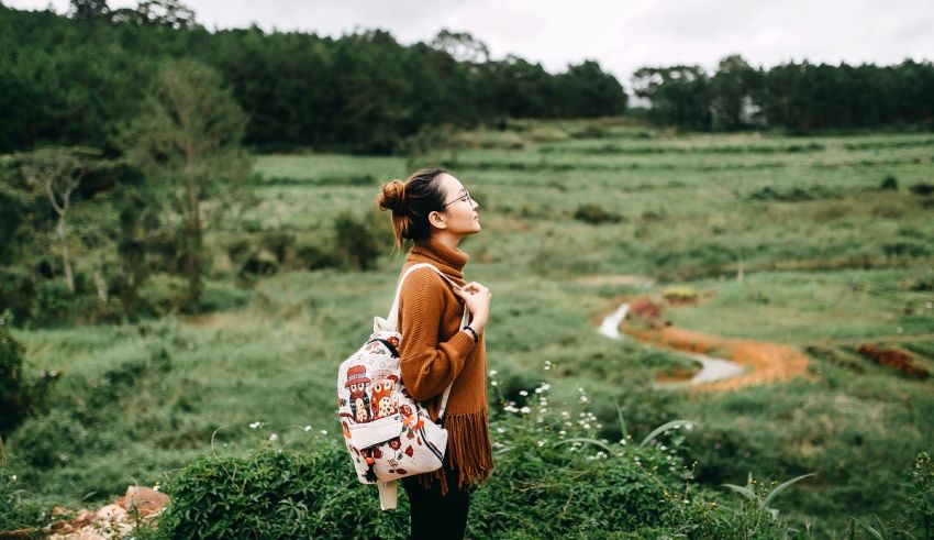 A woman standing in a field with a backpack.