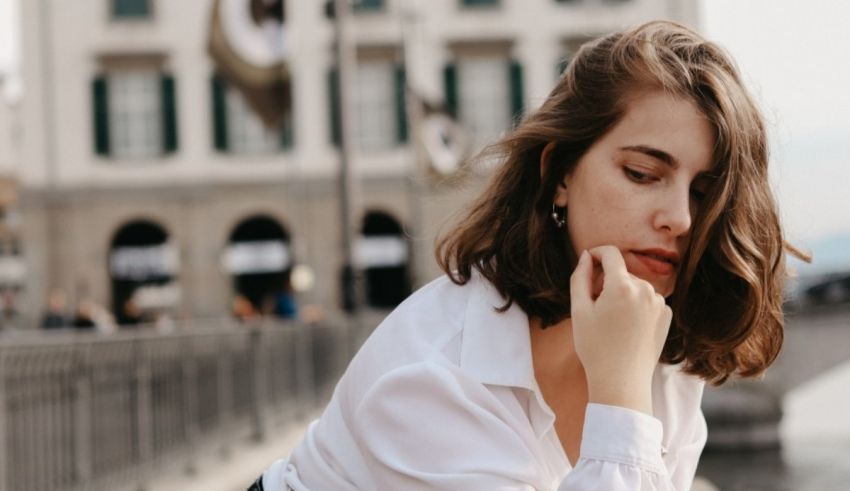 A woman leaning against a wall with her hand on her chin.