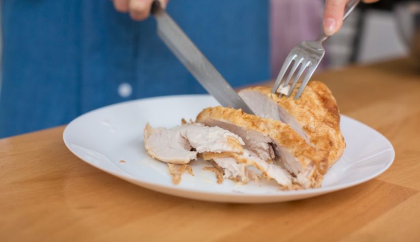 A person cutting a piece of chicken on a plate.