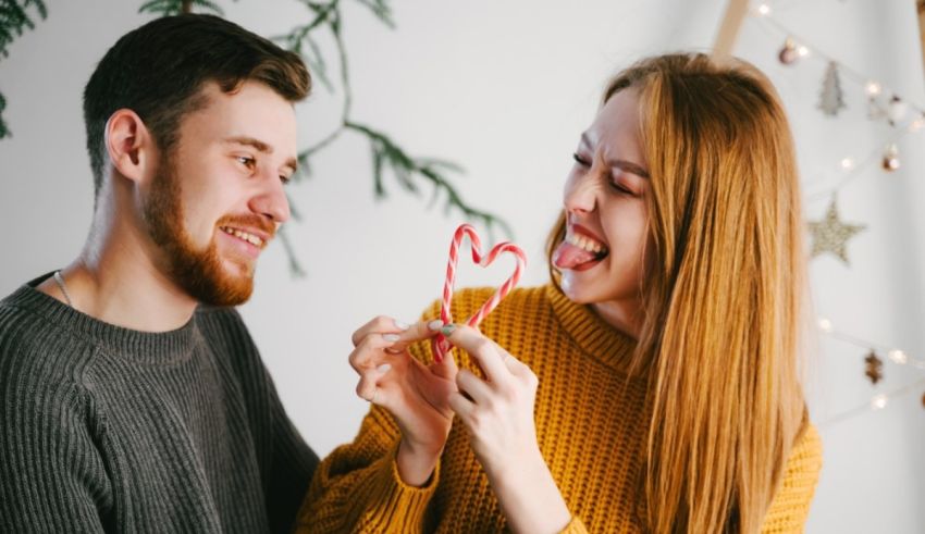 A couple holding a candy cane in front of a christmas tree.