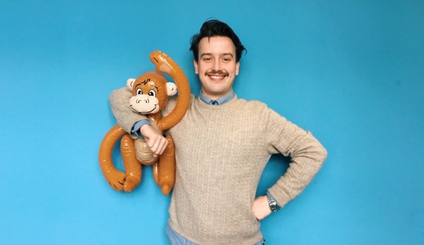 A man holding a stuffed monkey against a blue background.