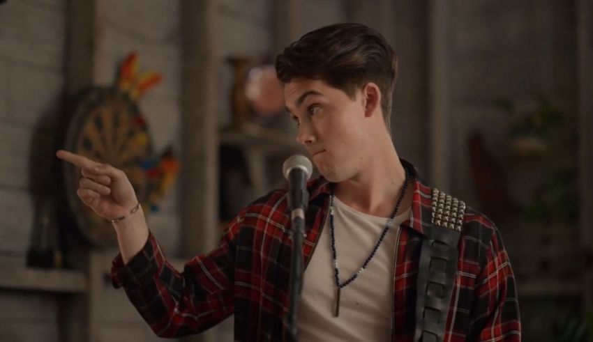 A young man in a plaid shirt is pointing at a microphone.