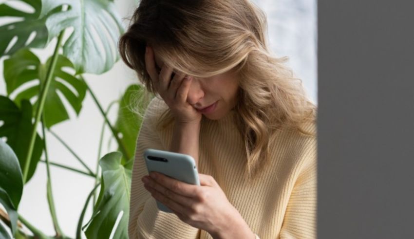 A woman is looking at her phone while sitting in front of a plant.