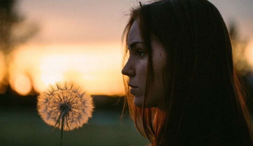 A woman is holding a dandelion at sunset.