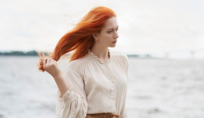 A woman with red hair standing by the water.