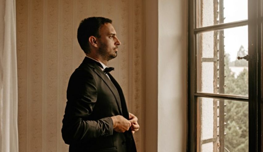 A man in a tuxedo standing by a window.
