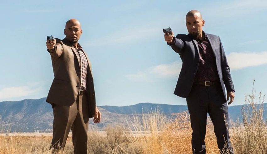 Two men in suits pointing guns in the desert.