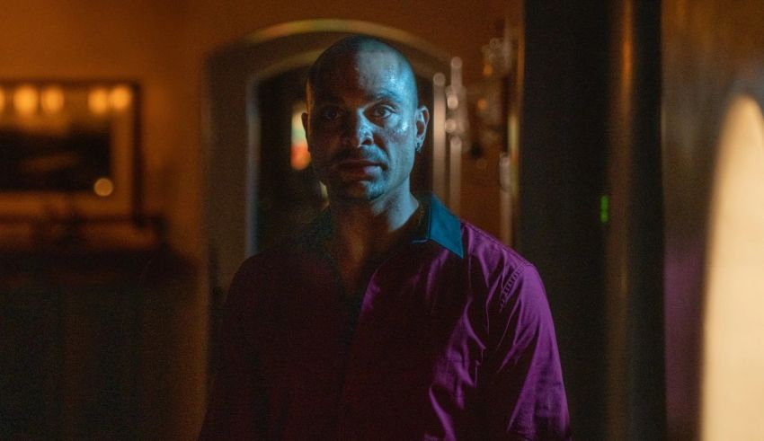A man in a purple shirt standing in a dark room.