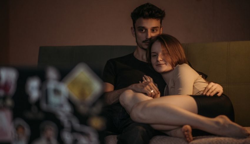 A man and woman sitting on a bed in front of a laptop.