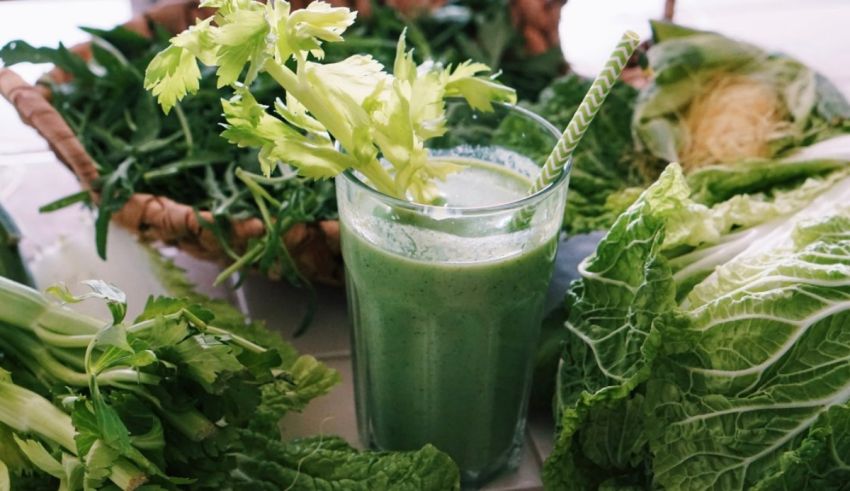 A glass of green smoothie next to a bunch of vegetables.