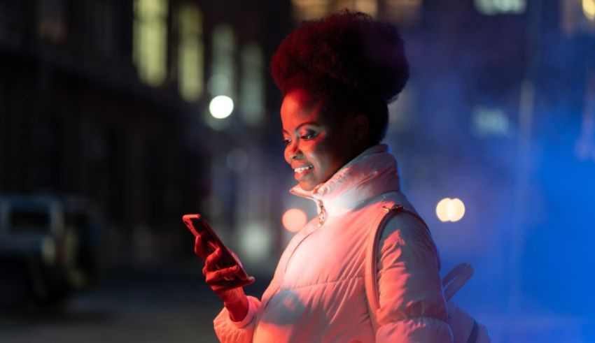 A young black woman using a cell phone in a city at night.