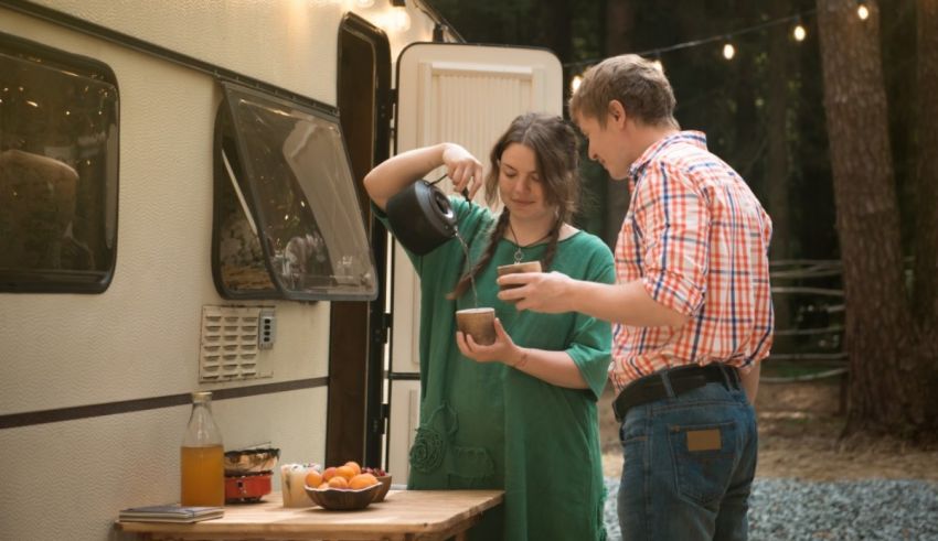 A man and a woman standing next to a camper trailer.