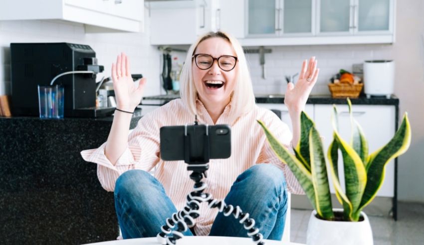 A woman is taking a selfie with a tripod in front of a potted plant.