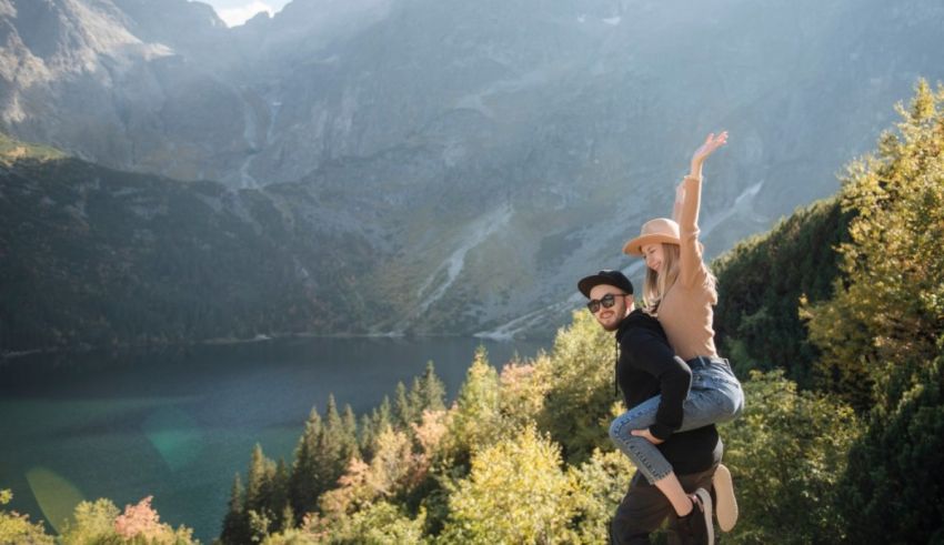 A couple is standing on top of a mountain overlooking a lake.