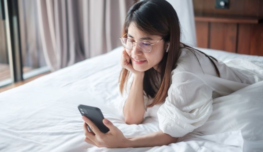 A young asian woman is laying on a bed and using her cell phone.