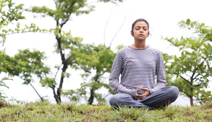 A woman is meditating in a field with trees.