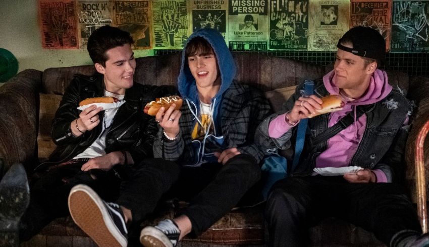 Three young men sitting on a couch eating hot dogs.