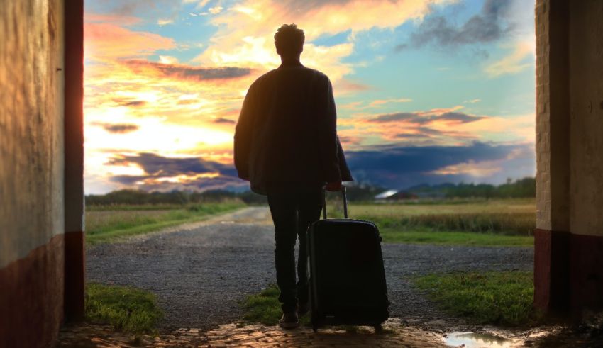 A man with a suitcase walking through an open door at sunset.