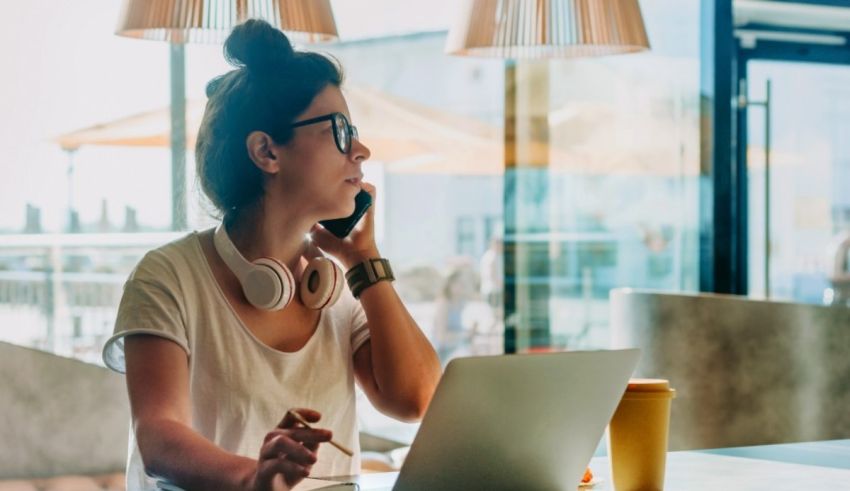 A woman talking on the phone while sitting at a table with a laptop.