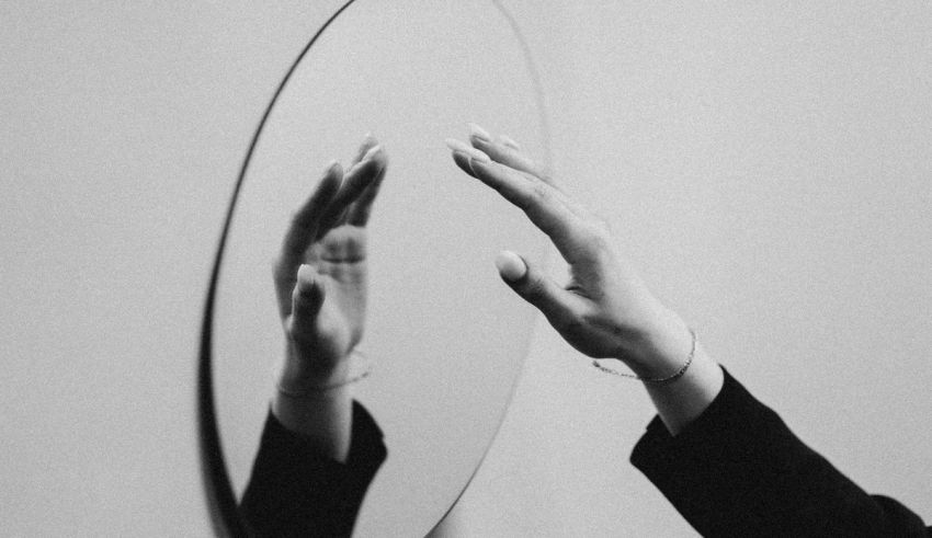 A black and white photo of a hand reaching into a mirror.