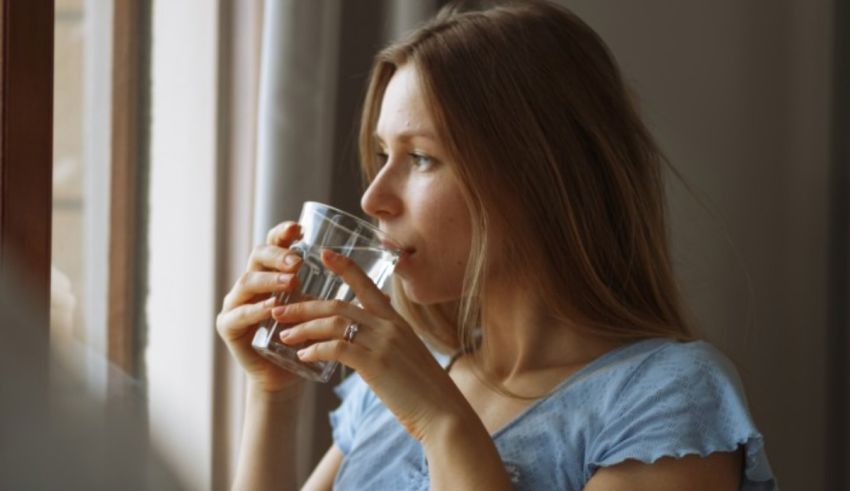 A woman drinking water out of a glass in front of a window.